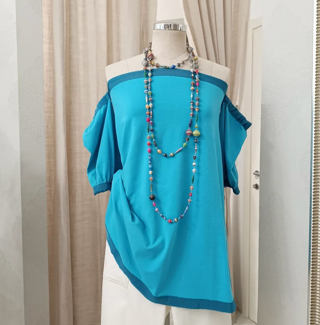 Blue top with colorful beads on a mannequin against a neutral curtain background