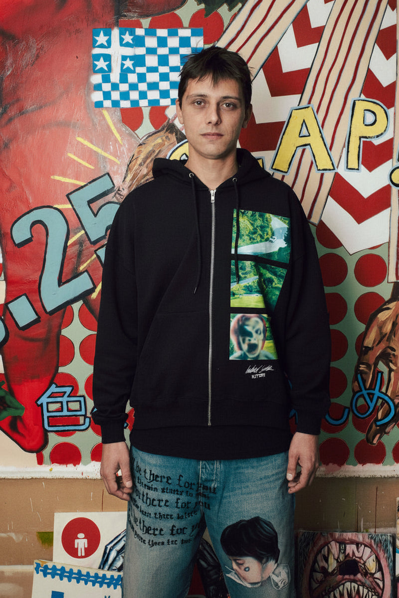Person wearing a black hoodie with a colorful graphic design in front of a vibrant, multicolored wall.