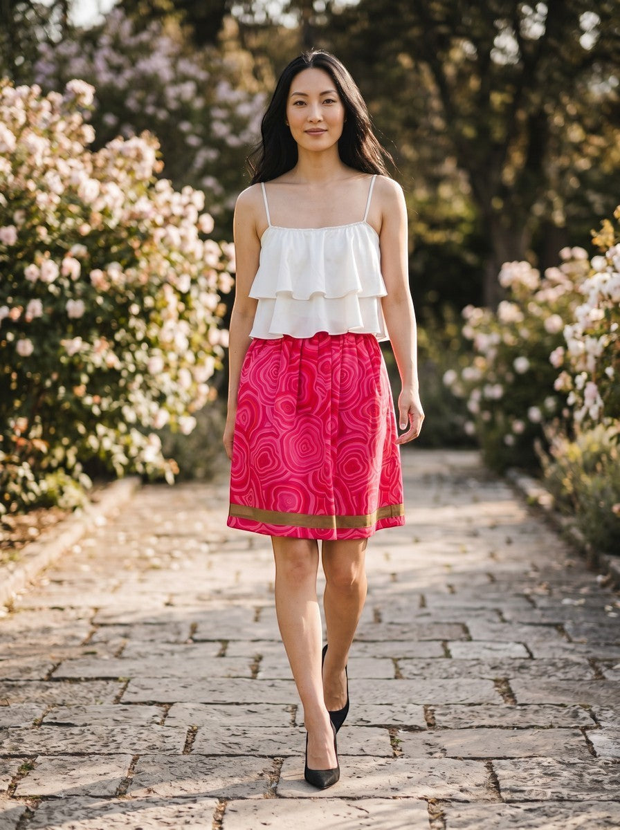 Modella indossa gonna a pieghe Invogue Again rosa e rossa con motivo geometrico e nastro a contrasto in un giardino